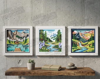 May include: Three framed landscape art pieces with white frames. Each piece depicts a layered paper art scene of mountains, trees, and water. One features a lake with a dock, another a river, and the third a waterfall. The art is displayed on a wooden shelf.