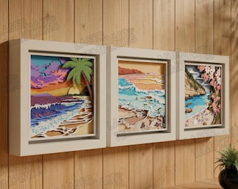 May include: Three framed layered paper art pieces depicting beach scenes. The artwork features colorful depictions of waves, sand, and sunsets, with a palm tree in one frame. The frames are white and mounted on a wooden wall.