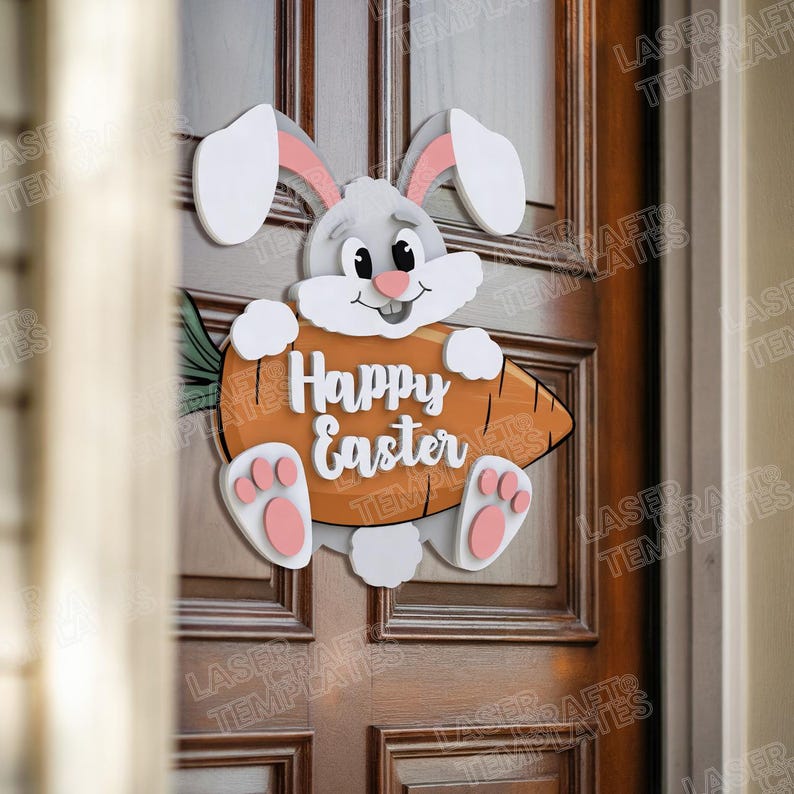 Pode incluir: Um coelho da P&aacute;scoa de madeira segurando uma cenoura com o texto "Happy Easter" nela. O coelho &eacute; branco com pelo cinza e orelhas e patas cor-de-rosa. A cenoura &eacute; laranja e tem folhas verdes.