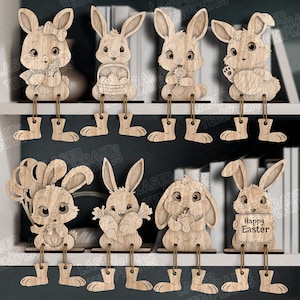 Könnte beinhalten: Eine Sammlung von acht hölzernen Osterhasen-Dekorationen. Jeder Hase ist aufwendig aus Holz geschnitten und hat hängende Beine. Die Hasen halten verschiedene Gegenstände, darunter Blumen, Karotten und Luftballons. Ein Hase hält ein Schild mit "Happy Easter".