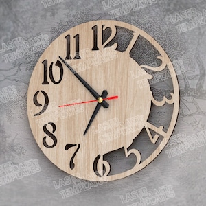 Puede incluir: Un reloj de madera redondo con un acabado de veta de madera clara. La esfera del reloj presenta grandes números negros y manecillas negras con un segundero rojo. El diseño incluye un recorte decorativo en el lado derecho. Aproximadamente 25 cm de diámetro.