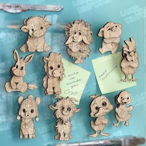 Op de afbeelding: Een verzameling van tien lasergesneden houten dierenmagneten, waaronder een Schotse hooglander, schaap, varken, ezel, pony, kip, lama, geit, eend en kuiken. Twee lichtgroene plakbriefjes zijn inbegrepen met de teksten 'A surprise awaits you' en 'Good morning'.