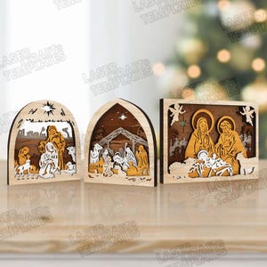 Puede incluir: Tres decoraciones de escena de la natividad de madera. Cada pieza presenta un diseño en capas con figuras y elementos arquitectónicos. La paleta de colores incluye tonos de madera natural, blanco y dorado, creando una estética cálida y festiva. El texto "LASER CRAFT TEMPLATES" es visible.