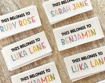 May include: A stack of white rectangular labels with colorful text that reads "This belongs to" followed by a name. The names are Ruby Rose, Sarah Jane, Luka Lane, and Benjamin.