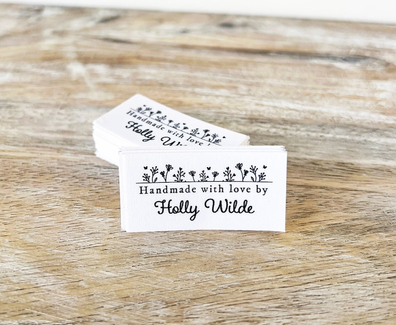 Puede incluir: Una pila de etiquetas rectangulares blancas con texto negro y un dise&ntilde;o floral. El texto dice "Handmade with love by Holly Wilde".