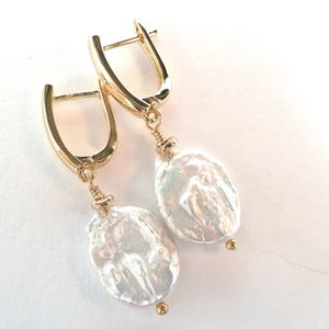 May include: Gold-tone hoop earrings with large, irregular-shaped white pearls. The earrings have a simple, elegant design with a small gold bead at the bottom of each pearl. The pearls have a lustrous, iridescent sheen.