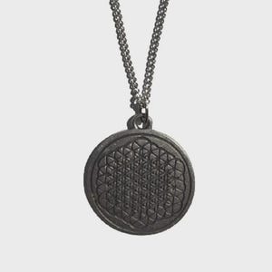 Puede incluir: Un collar de cadena de plata con un colgante redondo que presenta un diseño geométrico. El colgante es de color plateado y tiene un patrón detallado.