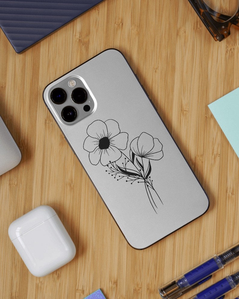 May include: A white phone case featuring a black outline of two flowers and leaves. The phone case has a camera lens cutout with three black circles.