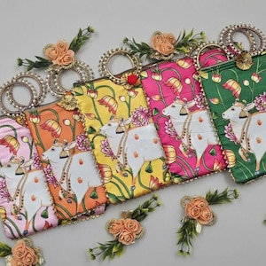 Può includere: Una collezione di pochette colorate e decorate. Ogni borsa presenta un'illustrazione di una mucca bianca con motivi floreali e a foglie. Le borse hanno manici color oro e sono decorate con accenti floreali. I colori includono rosa, arancione, giallo e verde.