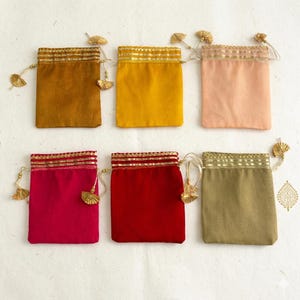 Può includere: Sei sacchetti colorati con coulisse nei toni del senape, pesca, rosso e verde oliva. Ogni sacchetto ha un bordo dorato e un nappa decorativa. I sacchetti sono realizzati in un tessuto morbido, ideali per piccoli regali o gioielli.