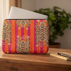 May include: A laptop sleeve with a striking tiger print. The sleeve has a quilted design with vertical orange and pink stripes. Black tigers are printed on the front. A laptop is partially visible inside the sleeve.