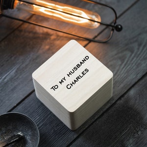 May include: A small wooden box with the text "To my husband Charles" engraved on the top. The box is sitting on a dark wood surface.