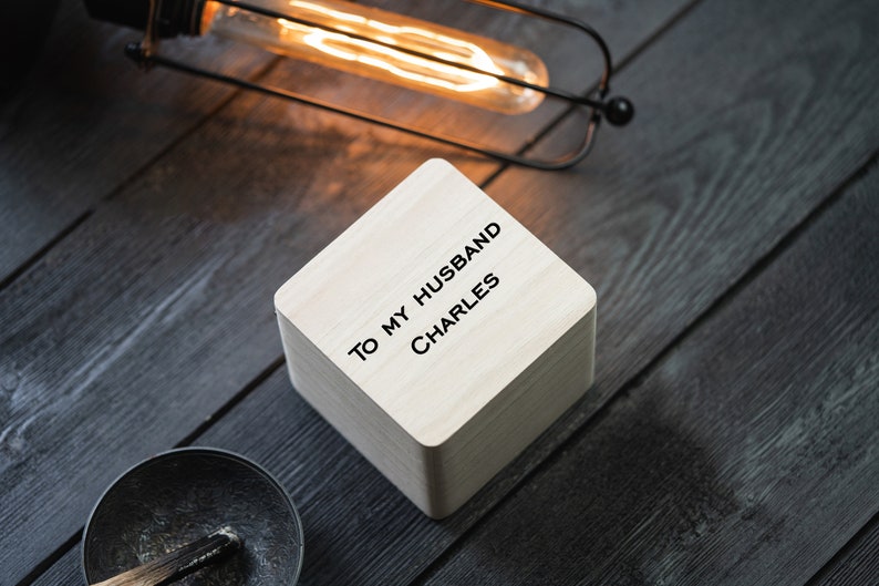 May include: A small wooden box with the text "To my husband Charles" engraved on the top. The box is sitting on a dark wood surface.