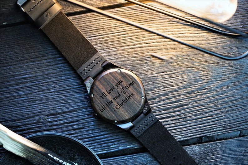 May include: A wooden wristwatch with a brown leather band. The watch face is engraved with the message "I'll love you till the end of time - Christina".