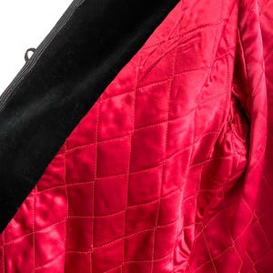 May include: Close-up of a black velvet jacket with a vibrant red quilted lining. The lining features a diamond pattern, and the jacket has black corded trim and small loops.