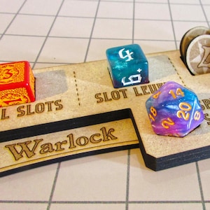 Może przedstawiać: Drewniana plansza do gry z miejscami na kości i żetony, oznaczona jako "Warlock", "Spell Slots" i "Mystic Arcan". Kolorowe kości z różnymi liczbami są umieszczone na planszy, w tym kości czerwone, pomarańczowe, niebieskie i fioletowe. Są też drewniane żetony.