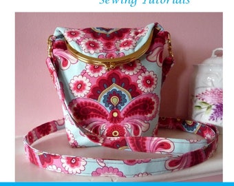 May include: A pink and blue floral patterned crossbody bag with a gold clasp. The bag has a long strap and is folded over at the top. The text "Fold Over Across the Body Bag" is at the bottom of the image.