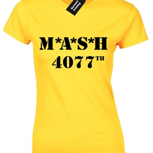 May include: A yellow t-shirt featuring the text "M*A*S*H 4077TH" in black. The top has a crew neck and short sleeves. A black tag with "Garment Printing" is attached. The shirt is a classic fit.