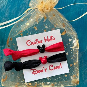 May include: Two hair ties with Mickey Mouse ears, one red and one black, in a gold star-patterned organza bag. The card reads "Cruise Hair Don't Care!"