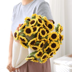 Peut inclure: Un bouquet de tournesols crochetés avec des pétales jaunes et des centres bruns. Les fleurs sont maintenues dans une enveloppe crochetée blanche. Les tournesols ont des feuilles vertes crochetées.