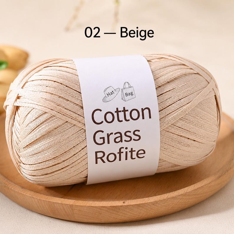 May include: A ball of beige ribbon yarn with a white paper label featuring the text 02 - Beige, Cotton Grass Rofite, and small line drawings of a hat and a bag. The yarn is wound into an oval shape and has a flat, smooth, and matte texture.
