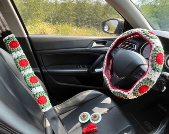 May include: A car interior with a crocheted steering wheel cover, seatbelt cover, and two small crocheted coasters. The steering wheel cover is red, white, and green, and the seatbelt cover is red and white. The coasters are red and white.