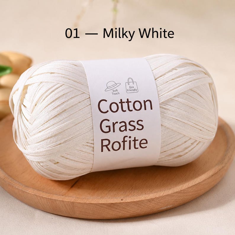 May include: A ball of milky white Cotton Grass Rofite yarn wrapped in a paper label. The label features the text 01 &mdash; Milky White, Cotton Grass Rofite, and icons of a hat and a shopping bag with the words Soft Touch and Eco Friendly.