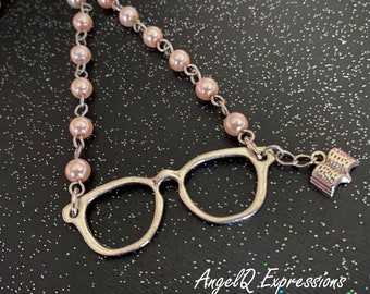 Può includere: Un ciondolo in argento con un paio di occhiali e un ciondolo a forma di libro. La collana è realizzata con una catena in argento e perline di perle rosa.