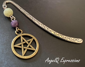Può includere: Un segnalibro in metallo color argento con un manico curvo e un motivo a onde inciso. In cima è fissata una catenella con una perla verde pallido, una perla viola e un ciondolo circolare a forma di pentagramma color bronzo. Il testo AngelQ Expressions è visibile.