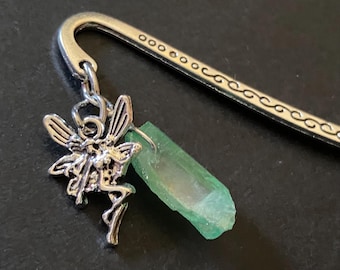 Può includere: Un segnalibro in metallo color argento con un'estremità curva decorata da un motivo a volute e una serie di piccoli cerchi. Un ciondolo a forma di fata color argento e una punta di cristallo verde traslucido grezzo sono fissati all'anello.