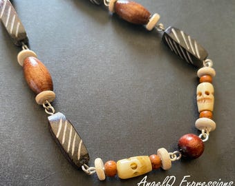 Può includere: Una collana caratterizzata da una sequenza di perline rettangolari marrone scuro con strisce diagonali bianche, perline ovali marrone liscio, piccoli distanziatori a disco color crema e perline a forma di teschio color crema collegate da anellini in metallo argentato.
