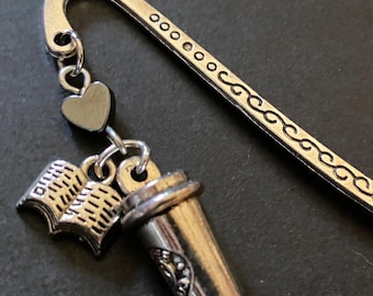 Può includere: Un segnalibro in metallo color argento a forma di gancio con un motivo a volute decorativo sul gambo. Al gancio sono appesi tre ciondoli: un piccolo cuore pieno, un libro aperto con pagine visibili e una tazza da caffè. Il testo AngelQ Expressions è visibile.