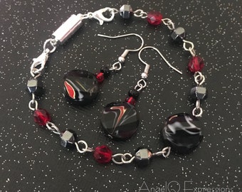 Può includere: Un braccialetto a catena argentata con perline rosse e nere, un paio di orecchini a spirale neri e bianchi con ganci argentati e una chiusura magnetica.