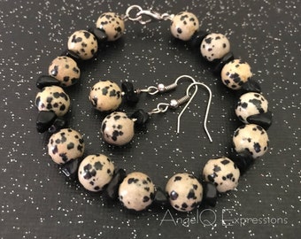 Può includere: Un set di gioielli composto da un braccialetto e orecchini. Il braccialetto è realizzato con perline di diaspro dalmata bianco e nero e perline di onice nero. Gli orecchini sono realizzati con onice nero e perline di diaspro dalmata con ganci d'argento.