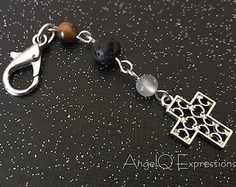 Può includere: Un braccialetto in argento con un ciondolo a forma di croce, un bead di occhio di tigre, un bead di roccia lavica e un bead di vetro trasparente. Il braccialetto ha una chiusura a moschettone in argento.