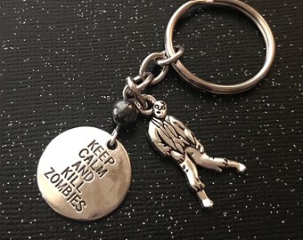 Può includere: Portachiavi in ​​argento con un ciondolo rotondo che dice "Keep Calm and Kill Zombies" e un piccolo ciondolo di zombie in argento.