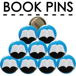 May include: A set of ten blue and white book-shaped pinback buttons. The buttons feature a white open book with black lines on a blue background. The buttons are arranged in a pyramid shape.