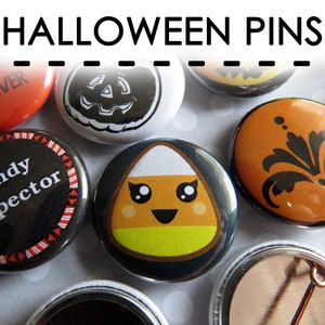 Puede incluir: Una colecci&oacute;n de pines redondos de Halloween con varios dise&ntilde;os, incluyendo un pin negro con el texto candy inspector, un pin con un personaje de ma&iacute;z dulce sonriente, un pin naranja con un patr&oacute;n floral negro y un pin rojo con texto.