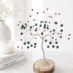 Könnte beinhalten: Eine Drahtbaumskulptur mit silberfarbenen Zweigen, die mit kleinen, runden, bunten Perlen in Magenta, Grün und Dunkellila verziert sind. Der Baum ist auf einem runden Holzsockel befestigt, der mit dem Text Happy 40th Anniversary beschriftet ist.