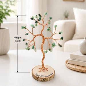 May include: A wire tree sculpture with copper-colored branches adorned with small green stone leaves. The tree stands on a round wooden base with bark edges, featuring the text "Happy 55th Anniversary" and a total height of 13 cm.