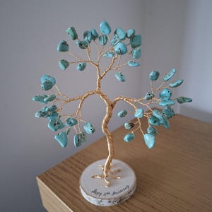 May include: A handcrafted tree sculpture with a gold wire trunk and branches, adorned with turquoise-colored stone leaves. The tree sits on a small, round wooden base with the inscription "Happy 11th Anniversary".