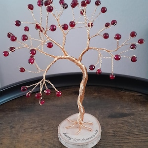 May include: A handcrafted copper wire tree sculpture with red bead accents. The tree is mounted on a clear, circular base with the inscription "Happy 40th Anniversary". A decorative item for home decor.