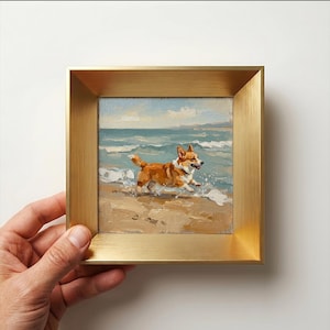 May include: A small square oil painting in a brushed gold metal frame depicting a brown and white Corgi dog running along a sandy beach with ocean waves in the background. The artwork features visible brushstrokes and a coastal scene.