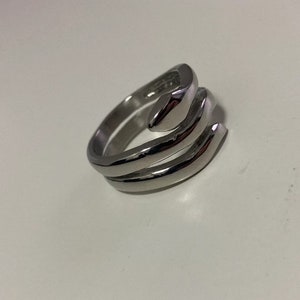 May include: A silver ring with a unique, abstract design. The ring is made of two bands that are twisted together, creating a three-dimensional effect.