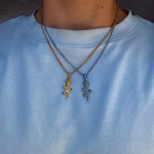 Könnte beinhalten: Zwei Halsketten mit Rosenanhängern. Eine Halskette ist goldfarben, die andere silberfarben. Beide Halsketten haben ein Kettenmuster. Die Anhänger sind mit einer Rosenform versehen. Die Halsketten werden vor einem weißen Hintergrund präsentiert.