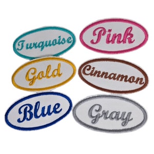 May include: Six oval-shaped fabric patches with embroidered text in different colors. The colors are turquoise, gold, pink, cinnamon, blue, and gray.