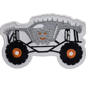 May include: White embroidered patch of a monster truck with a silver body, black tires with orange rims, and a grinning monster face.