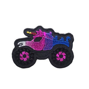 May include: A black monster truck with pink and blue glitter accents. The truck has a unicorn horn and a large, pink flower on the front.