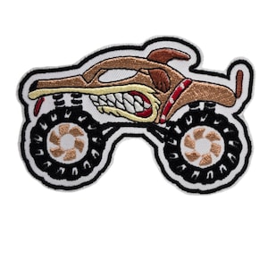 May include: Embroidered patch of a brown monster truck with a dog's head, wearing a red collar with white polka dots. The truck has large black tires with brown rims and white spokes.