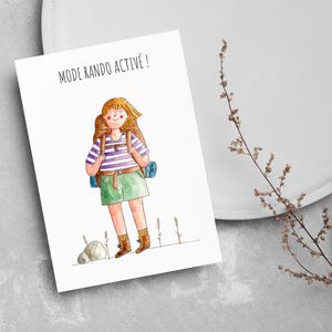 Peut inclure: Illustration à l'aquarelle d'une personne avec un sac à dos, portant un t-shirt rayé, une jupe verte et des bottes. L'image comprend le texte "MODE RANDO ACTIVE!" sur une carte blanche, avec un fond gris et une brindille de fleurs séchées.